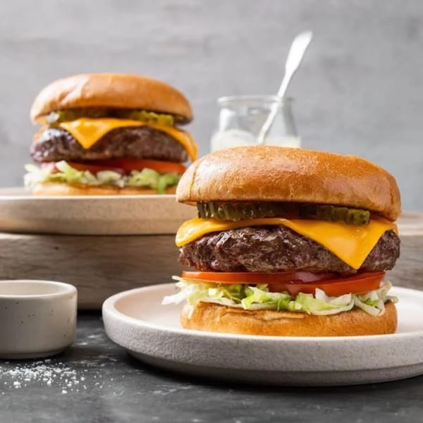 Two Firewater Sports Bar Cafe cheeseburgers with lettuce, tomato, and pickles on a dark surface.