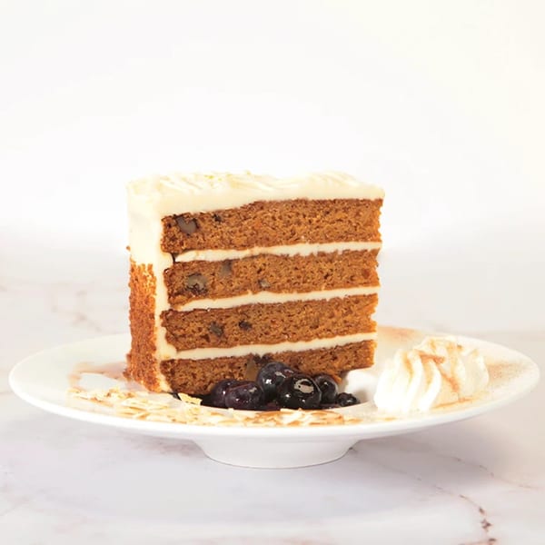 A slice of carrot cake with cream cheese frosting, blueberries, and whipped cream on a white plate.