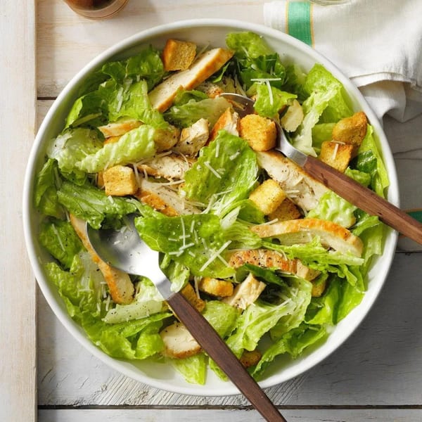 A large white bowl of Caesar salad with grilled chicken, croutons, and parmesan cheese.