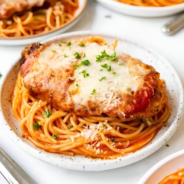 Chicken Parmesan with melted cheese and parsley, served over spaghetti with red sauce.